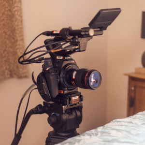A photograph of a camera next to the edge of a bed.