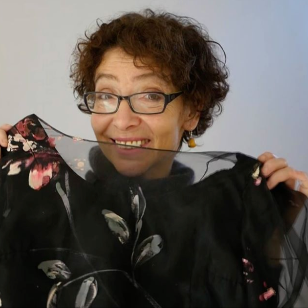 An older woman holds up a black vintage dress as she smiles.