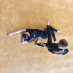 An overhead view of two girls dancing. One is lying outstretched on the floor, the other is stood up and stepping over her.