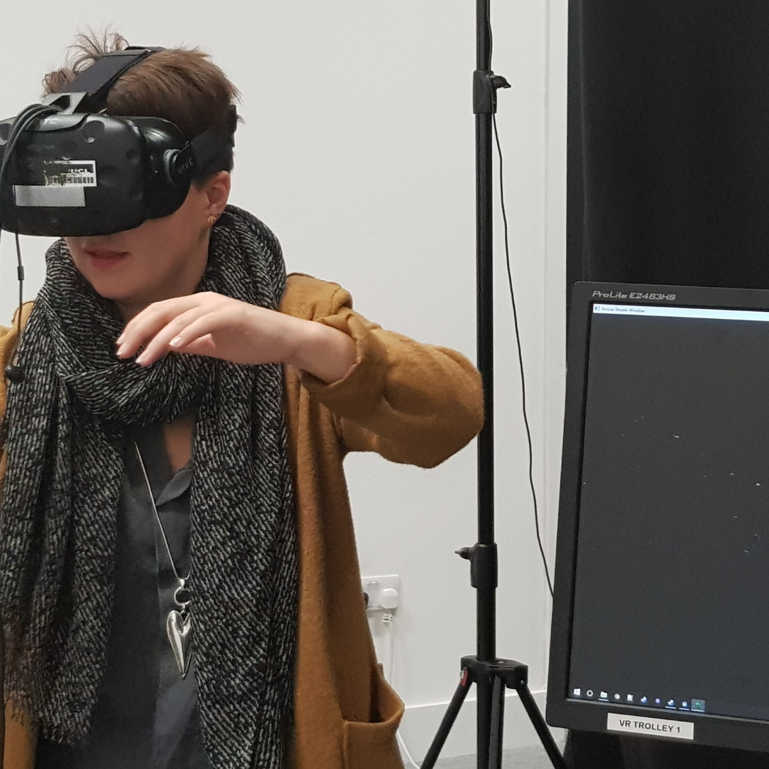 Artistic Director Katie is dancing whilst in VR. She has short brown hair and is wearing a black and white scarf and a burnt orange coat.
