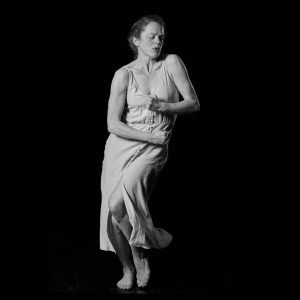 a black and white image of a woman posing for a picture in the dark with her arms wrapped around body