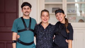 Three members of the KDE Dance team standing in a dance studio. On the left is Ed wearing a green t-shirt and jeans and in VR suit. In the middle is the Artistic Director Katie Dale-Everett wearing black trousers and navy blouse. On the right is Gabby in all black and in a VR suit.