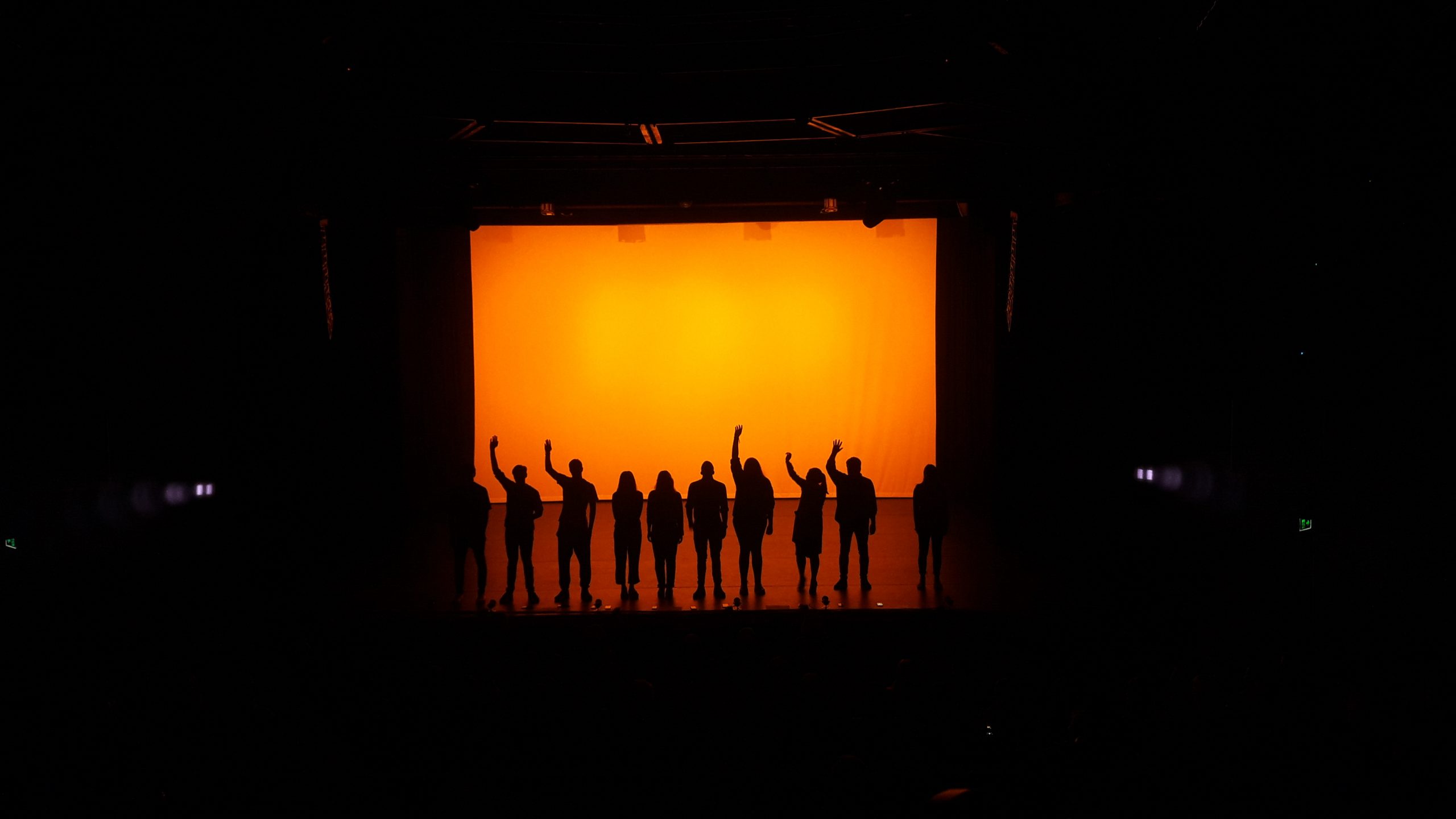 A group of people standing on top of a stage with an orange lit backdrop.