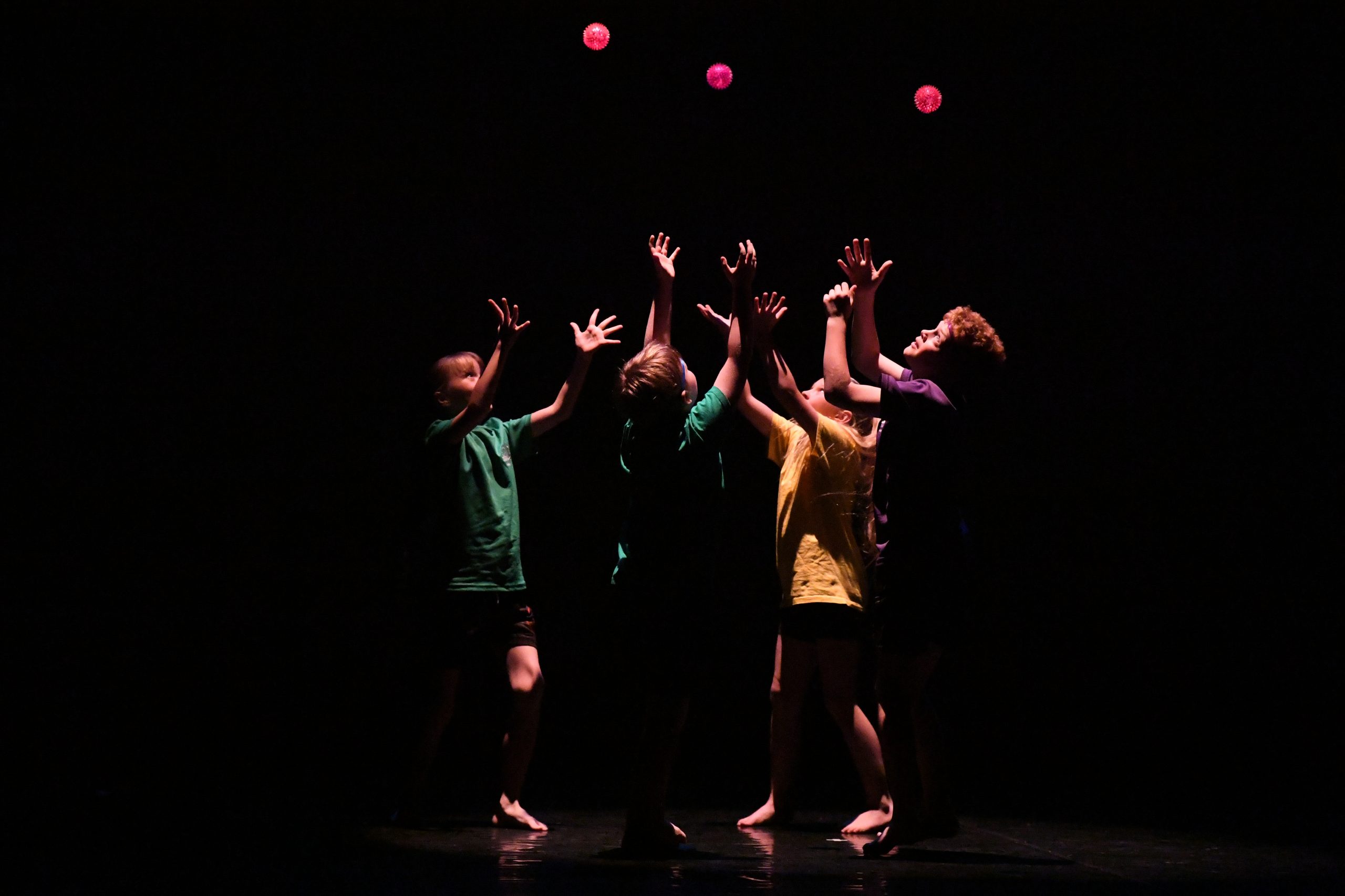 Group of children standing on stage throwing red balls in the air