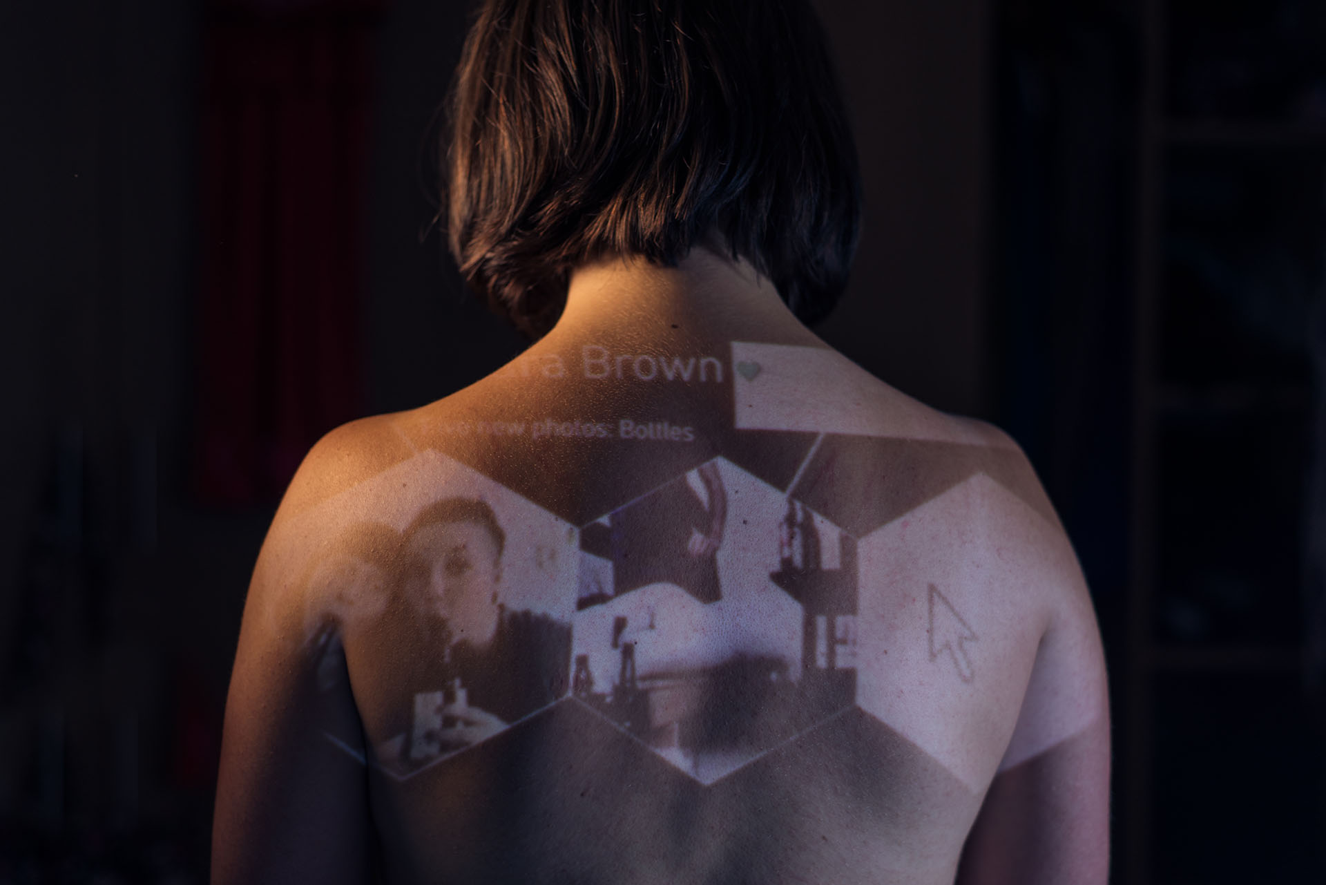 A person with their back to the camera. There are images being projected onto their skin.