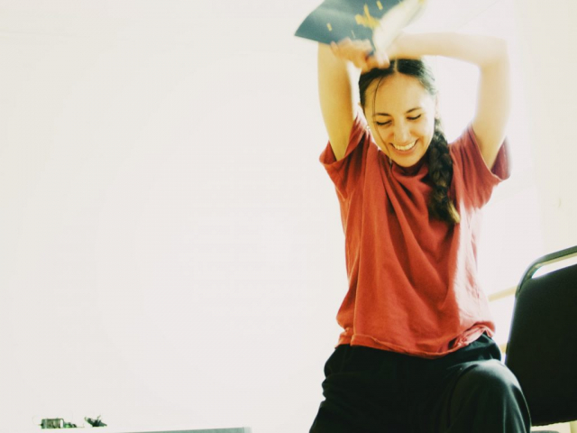 a person sitting on a stool reading a book with her hands in the air.