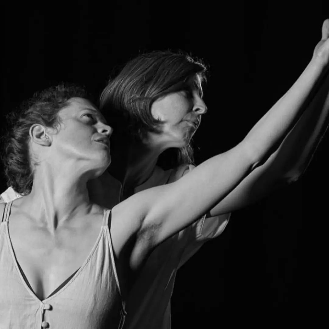 two women in a white shirt and one woman with hands in the air, black background