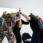 A photo of a group of people pressing their hands together as they lean forward.